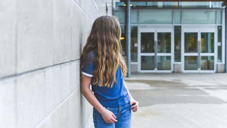 Teenage girl looking over her shoulder while leaning against a brick wall.