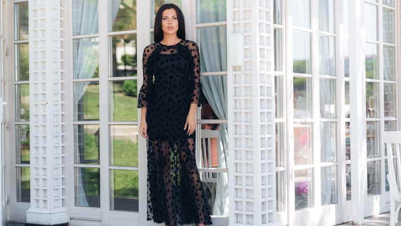 A tall slim model stands outside, dressed in a black tight-fitting mesh dress. Poses on the background of the stained-glass white doors. The concept of fashion, evening image, people, restaurants