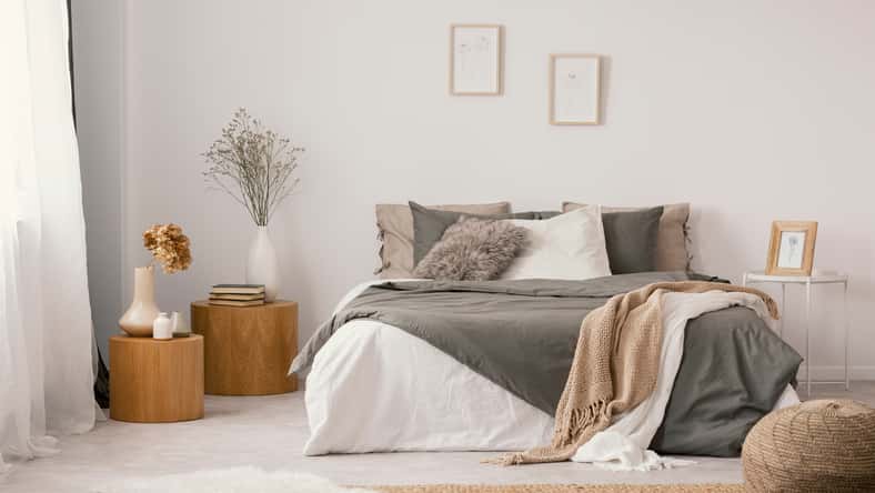 Flowers on wooden stool and pouf in white bedroom interior with posters above bed. Real photo