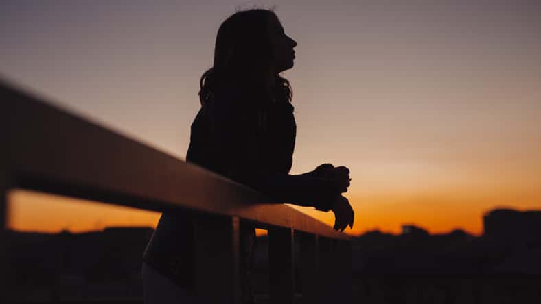 Silhouette of woman thinks and dreams about future at sunset in city