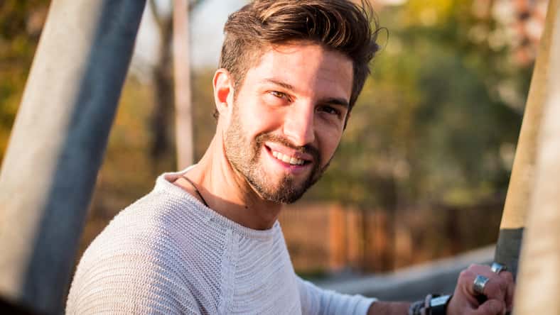 One handsome young man in urban setting in European city, standing and smiling to camera happy
