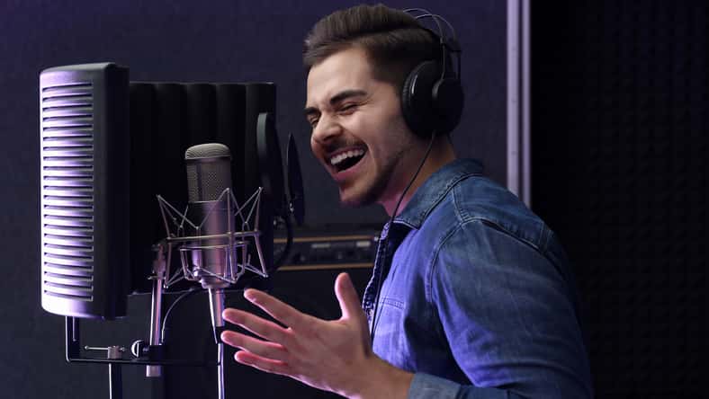 Young singer with microphone recording song in studio