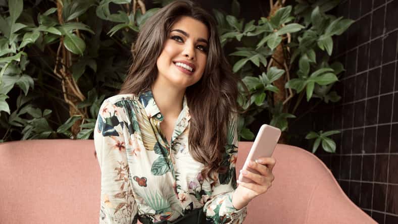 Young beautiful woman holding coffee cup and using mobile phone, sitting at cafeteria. Happy student girl using smartphone. Businesswoman drinking coffee and smiling.