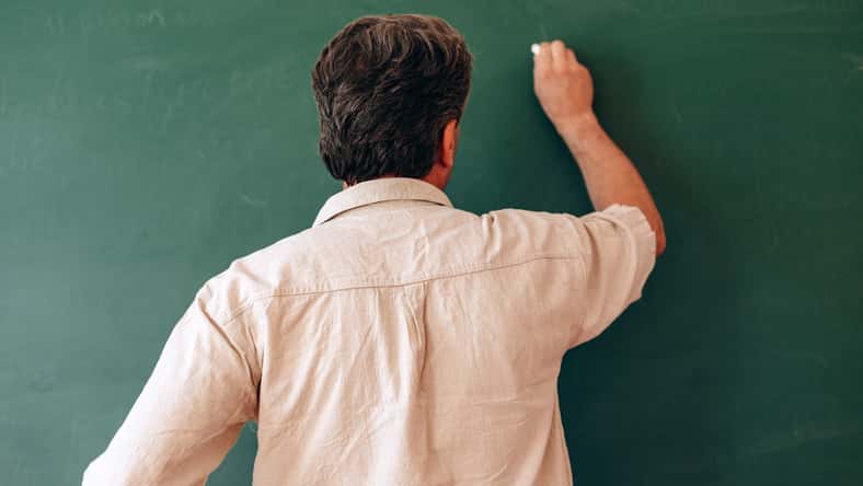 Teacher write on the blackboard and explain a lesson. Back view- Image