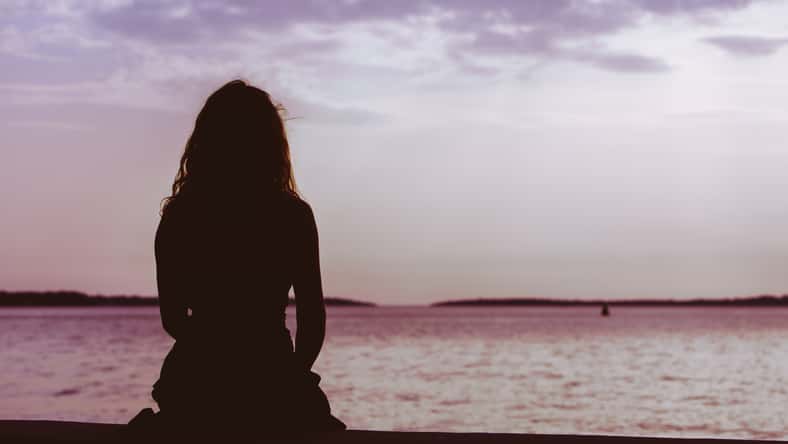 woman silhouette sitting on the beach looking at sunset over the sea. copy space