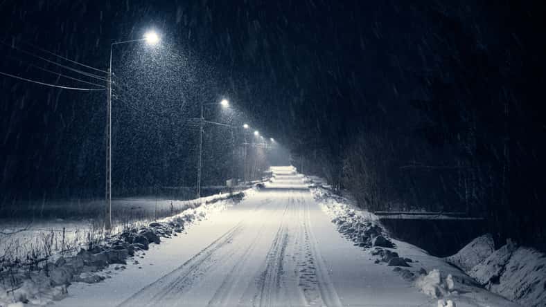 road in the blizzard snow in winter at night. In the light of lamps visible falling snow.