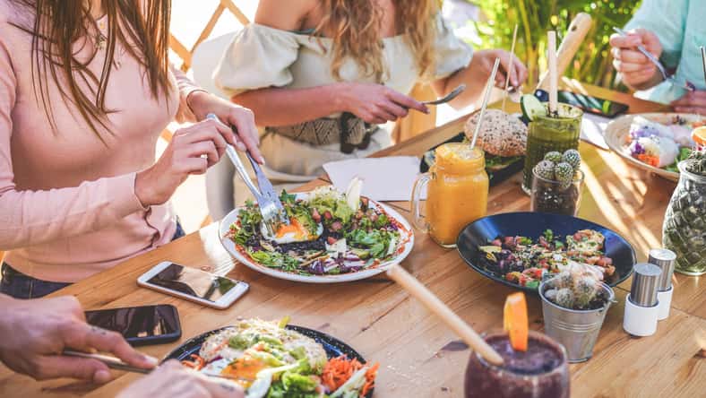 Hands view of young people eating brunch and drinking smoothies bowl with ecological straws in trendy bar restaurant - Healthy lifestyle, food trends concept - Focus on left woman hand, dish