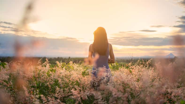 Trendy girl in stylish summer dress feeling free in the field with flowers in sunshine.