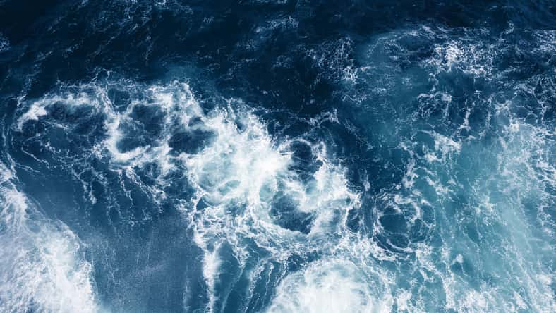 Top view on blue ocean waves and foam.