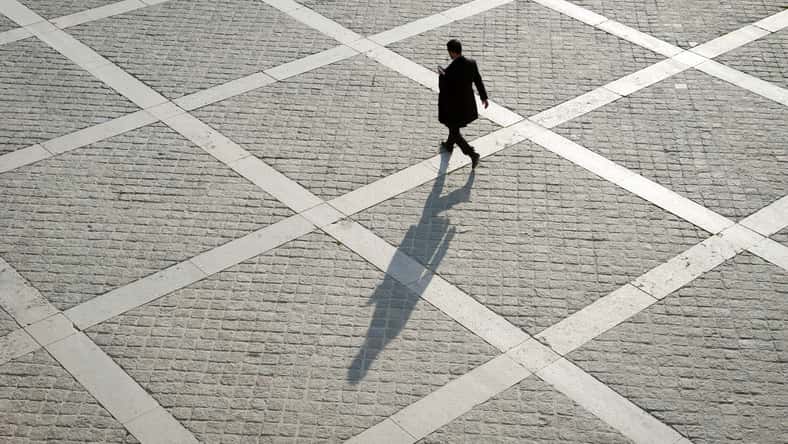 Overhead view of unrecognizable pedestrian casting shadow on the geometric patterns of a stone plaza on a quay next to the River Seine in Paris, France