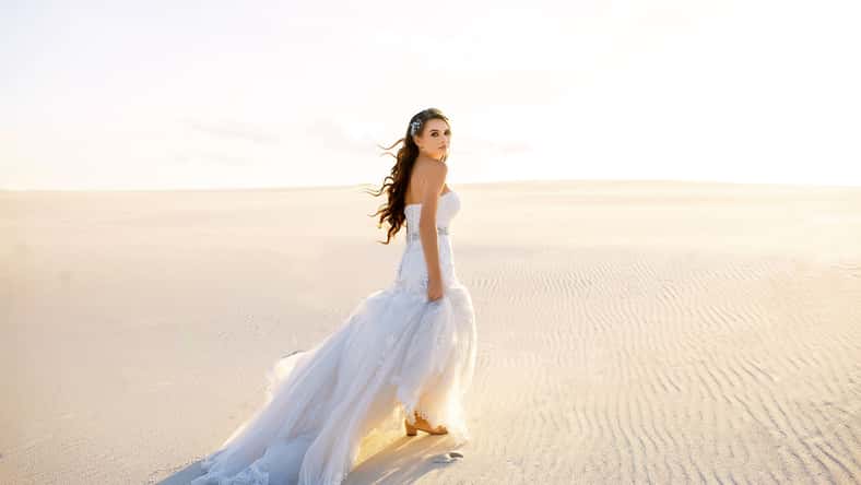 beautiful bride in a beautiful long dress walks on the sand in the desert, backlight, sunset, tender girl, designer wedding dress, a sense of freedom, the wind moves hair, desert dunes