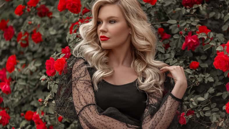 Beautiful blonde woman in garden with red roses. Spring time.