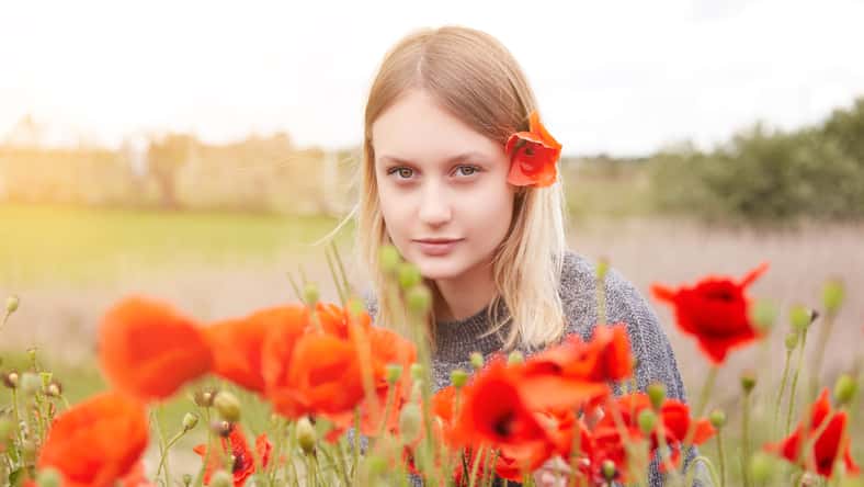 Beautiful young girl 18 years old blonde in a poppy field. Spring day in the village, a girl in the sun, a red poppy flower in her hair.