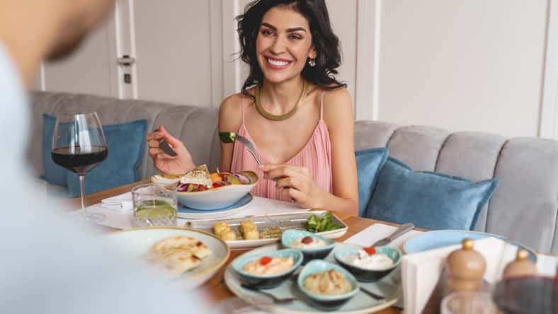 Attractive lady looking at man and smiling while sitting at the table with delicious food
