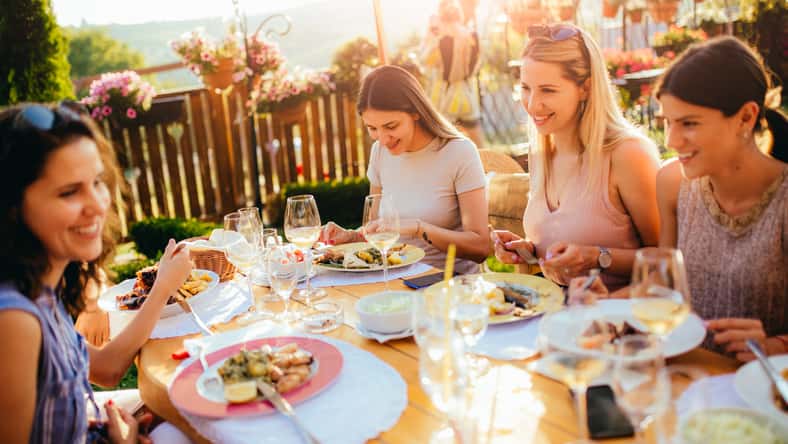 Young beautiful female friends are talking, eating, drinking and smiling while sitting at the table and having lunch