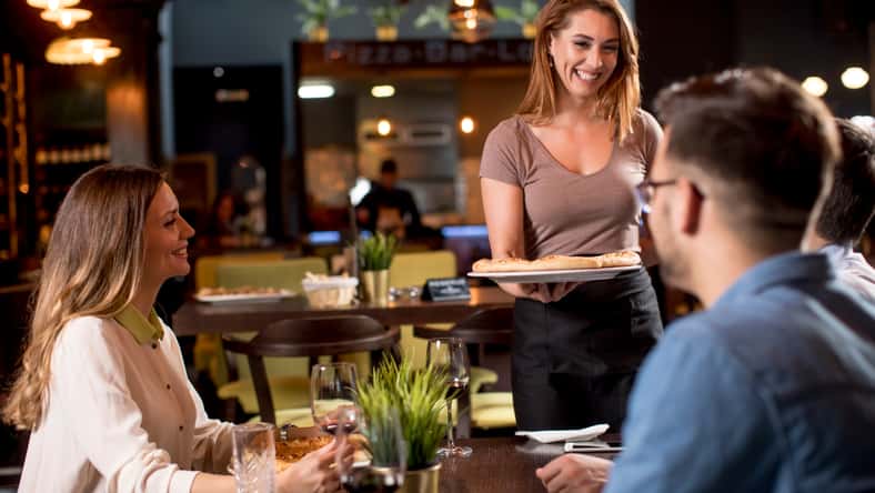 Pretty waiter woman serving group of friends with food in the restaurant