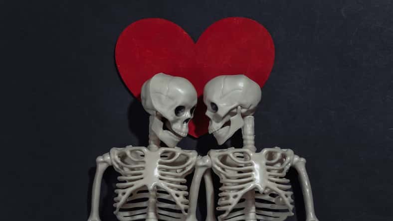 Couple of lovers skeletons and red decorative heart on black background. Valentine's day or halloween theme. Top view. Flat lay
