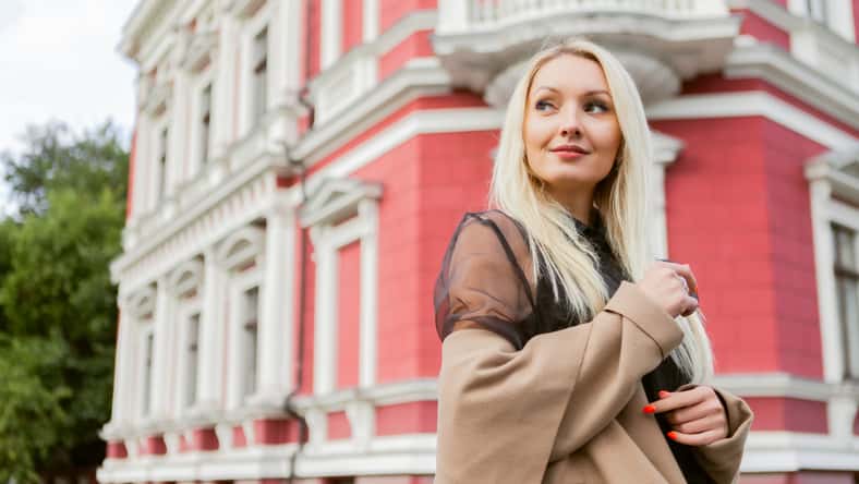Cute attractive fashion woman in autumn coat posing against the background of urban architecture. Street fashion