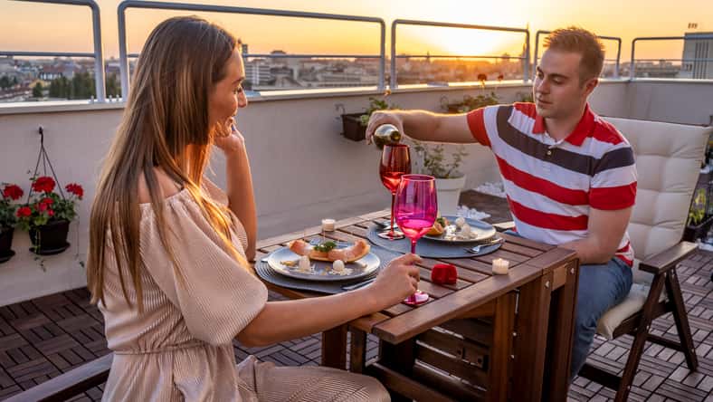 Beautiful young couple enjoying romantic dinner at roof top terrace drinking vine and eating food