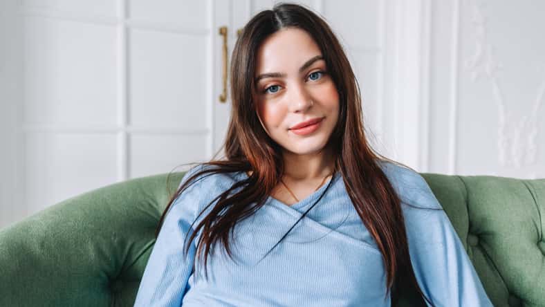 Portrait of attractive pretty young woman in casual clothing sitting on a sofa and looking on camera.