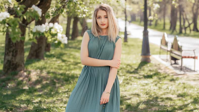 Beautiful blonde woman in a green long dress stays in a spring blooming garden.