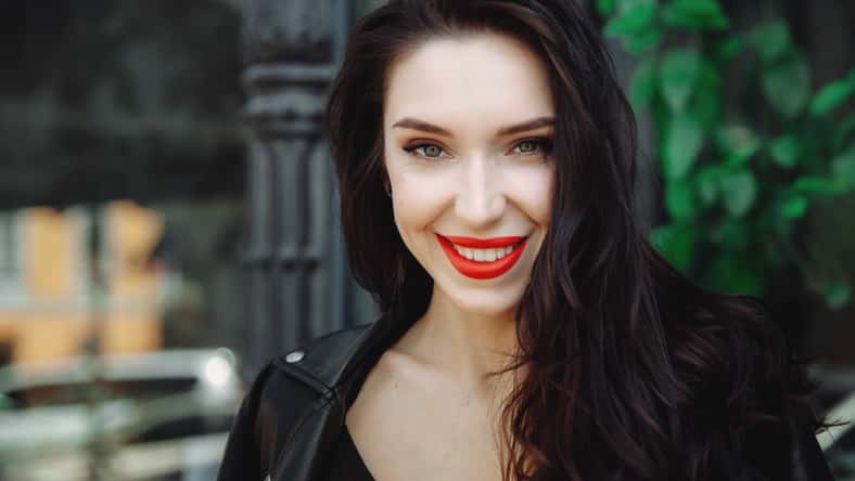 Amazing joyful pretty girl with long brunette hair wearing in leather jacket. Close up fashion portrait of pretty seductive young woman. Red lips, wavy hairstyle. Model smiling and looking at camera.