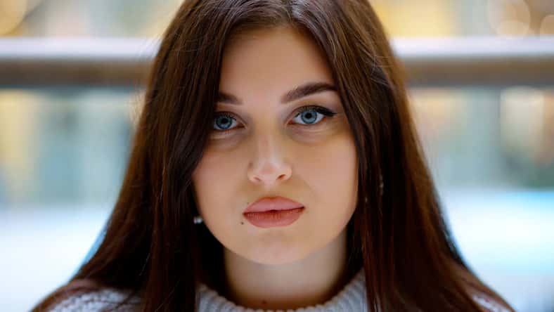 Mujer joven con cabello largo y ojos azules mirando la cámara, fondo borroso. Retrato de primer plano de la hermosa modelo femenina. Concepto de belleza