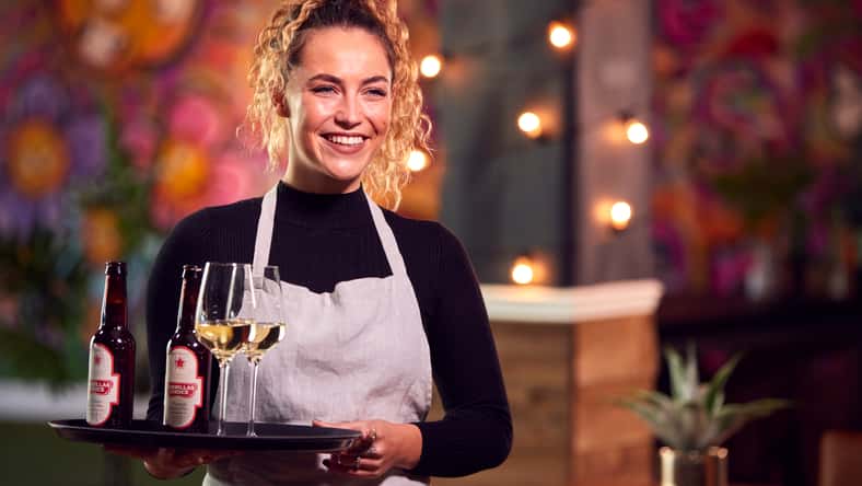Portrait Of Smiling Female Server Holding Tray Of Drinks In Cool Bar Or Club