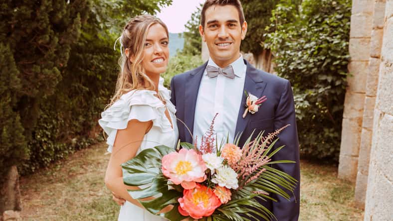 Beautiful wedding couple portrait. Bride and husband posing with a bouquet of flowers outdoors looking at camera.