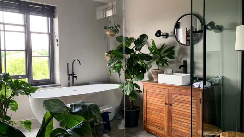 Charming cozy bathroom view. Bath tube by the window. Taking bath at home or in a hotel. Charming cozy indonesian style. Bathroom view. Home Plant in room.