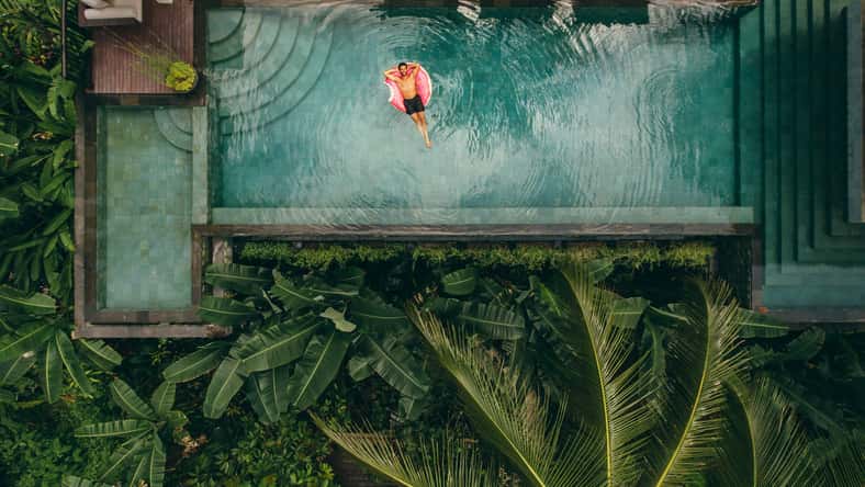 Aerial shot of young man relaxing in resort swimming pool. Male on inflatable ring in pool.