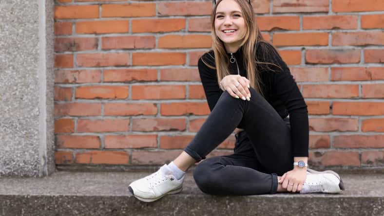 portrait of a cheerful cute smiling girl, 17 years old, with long hair and sunglasses on her head, in a black turtleneck, sits against the background of a brick wall