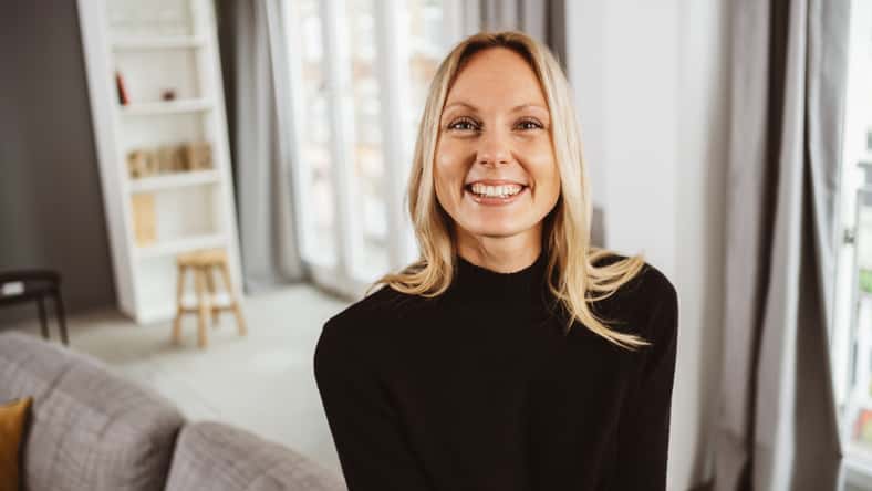 Laughing young blonde woman sitting on the sofa and looking at the camera