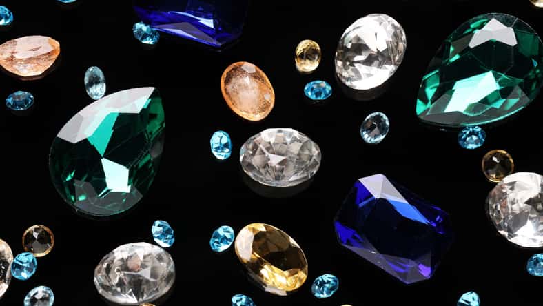 Different beautiful gemstones for jewelry on black background, flat lay