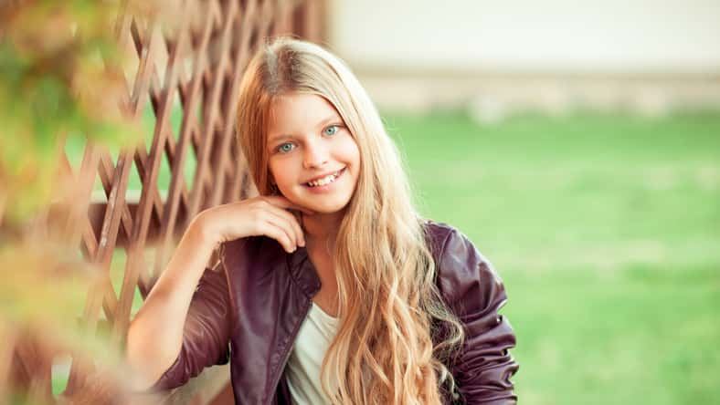 Smiling blonde teen girl 12-14 year old posing outdoors. Looking at camera.