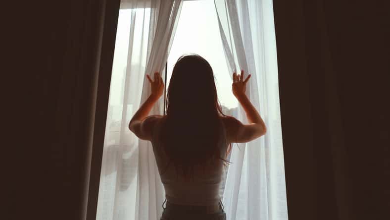 young woman opening curtains in a bedroom