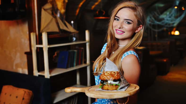 camarera de niña bonita sosteniendo una deliciosa hamburguesa en una bandeja sobre un fondo del restaurante