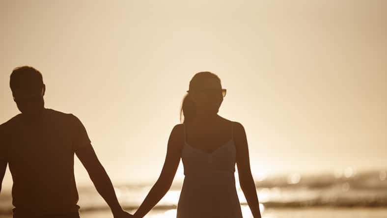 Walking, love or couple holding hands at beach for valentines day, sunset or romance. Summer vacation, silhouette or people bonding on holiday at sea in Spain for romantic honeymoon or travel date.