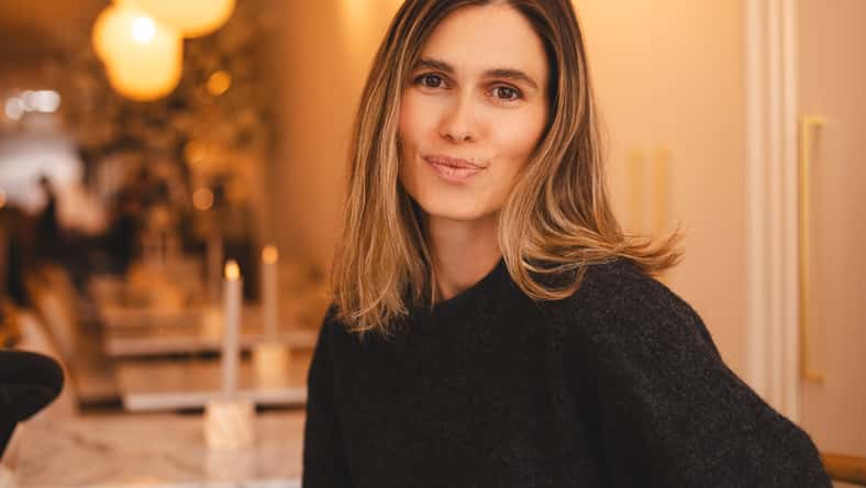 Happy young woman sitting on chair at cafe and looking at camera. Portrait of comfortable woman in wool warm sweater. Portrait of beautiful girl smiling, laughing and relaxing.