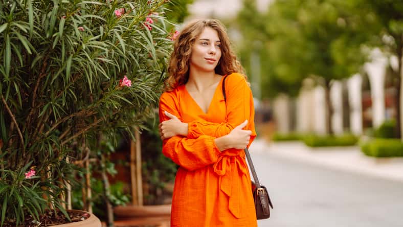 Cheerful tourist in a bright dress walks along a beautiful street. A young woman enjoys the weather outdoors. The concept of walking, vacation, travel. Active lifestyle.