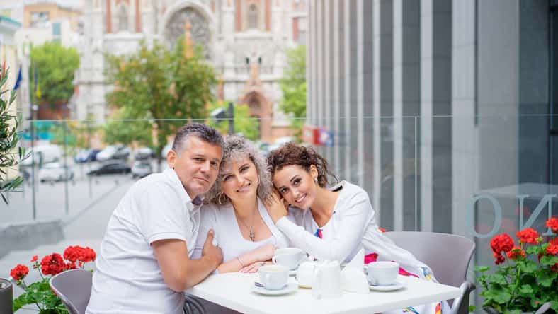 Family day. Elderly loving couple and their adult daughter smiling at camera while sitting in sidewalk cafe.