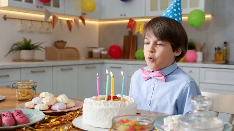 Cute little boy blowing out candles on birthday cake indoors. Surprise party