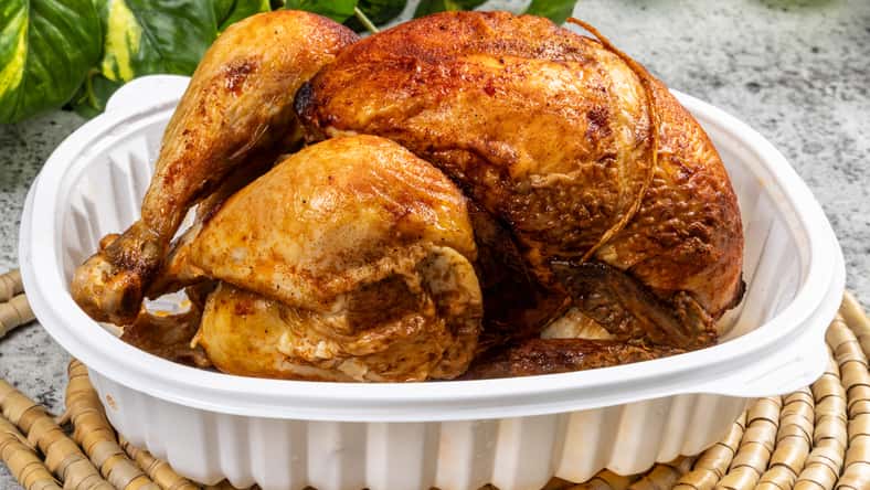 A whole rotisserie chicken in a take out pan