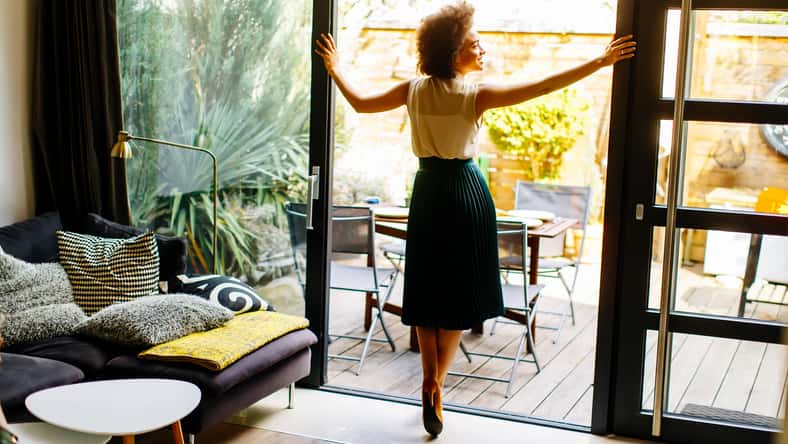Young woman with curly hair posing in the house next to the open glass door
