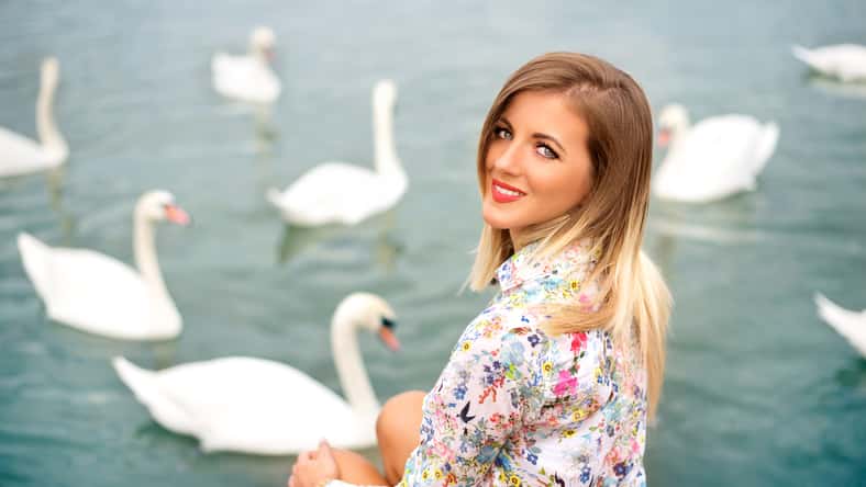 Beautiful blonde woman sitting on the beach with swans