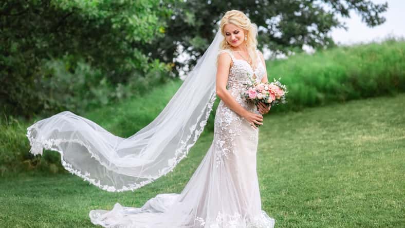 beautiful bride in wedding dress with long veil fluttering in the wind outdoors