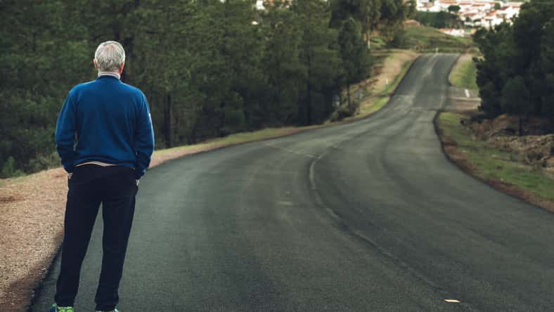 Active senior man standing on lonely road between mountains. Older man of back standing on lonely highway