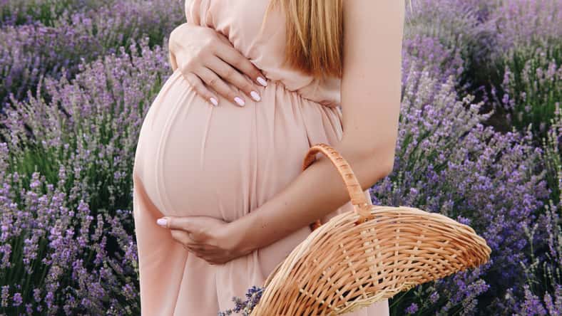 Pregnant girl blonde in a beige dress and straw hat. Lavender field. In anticipation of a child. The idea of a photo shoot. Walk at sunset. Future mom. Basket of flowers.