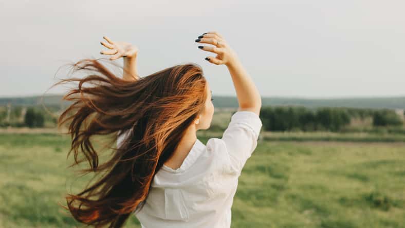 Close up portrait of beautiful long hair girl in white clothes in field, view from back. Sensitivity to nature concept