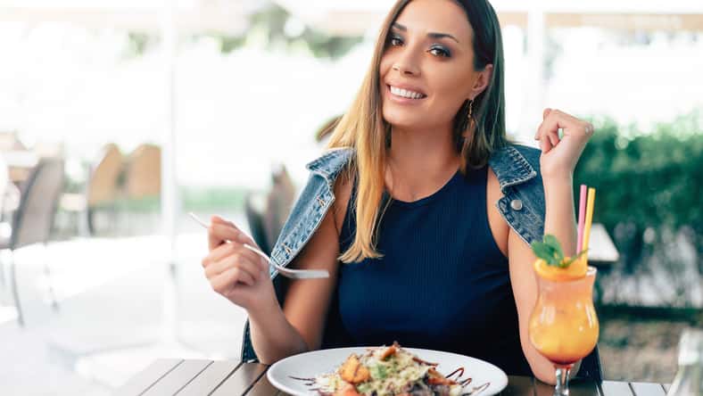 Beautiful young caucasian woman eating fresh caesar salad in an outdoor restaurant. Summer mood, enjoying food, happy people